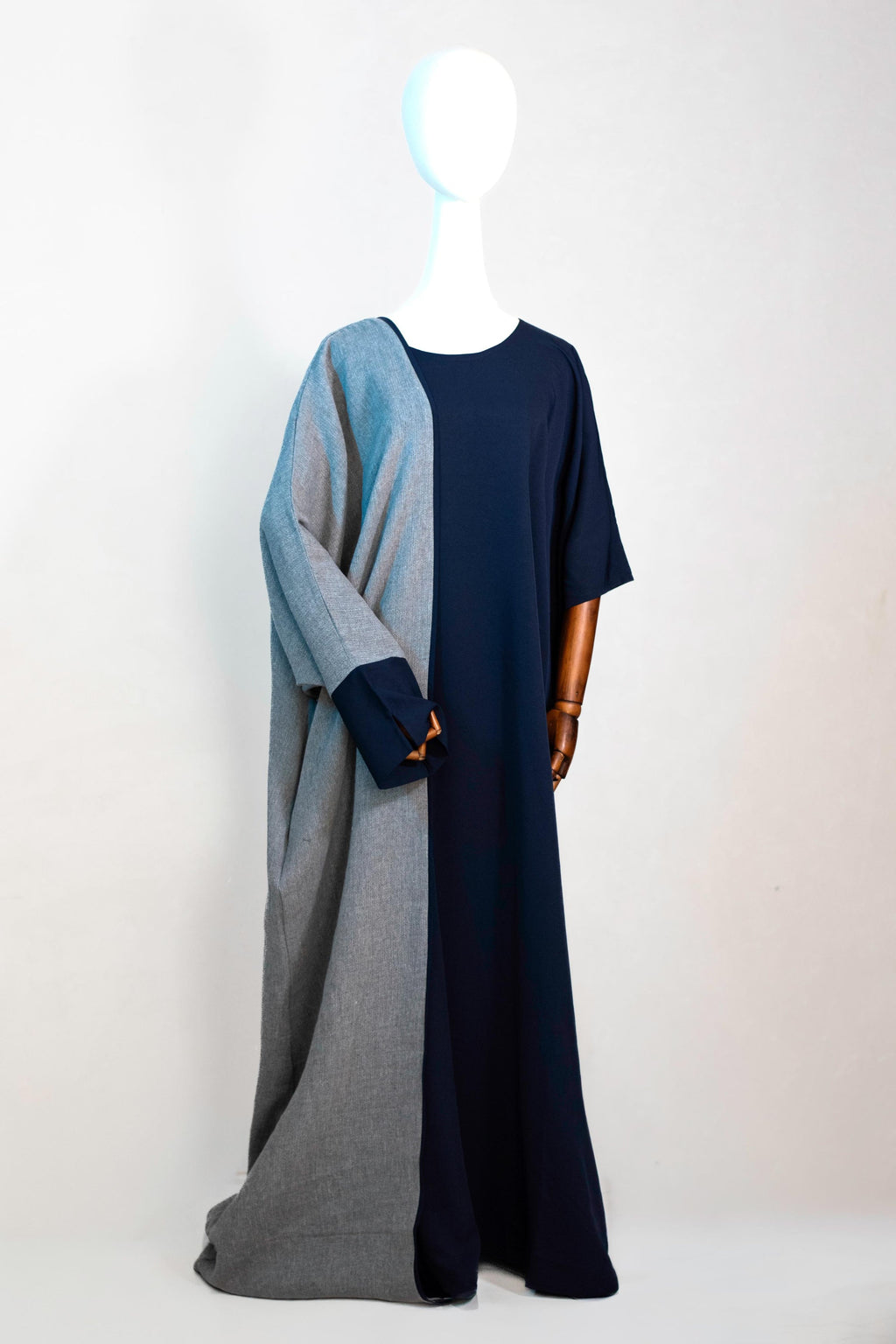 Grijze en marineblauwe abaya van Saahil Collection op houten mannequin, met wijde pasvorm en open voorkant, gefotografeerd tegen een lichte achtergrond.