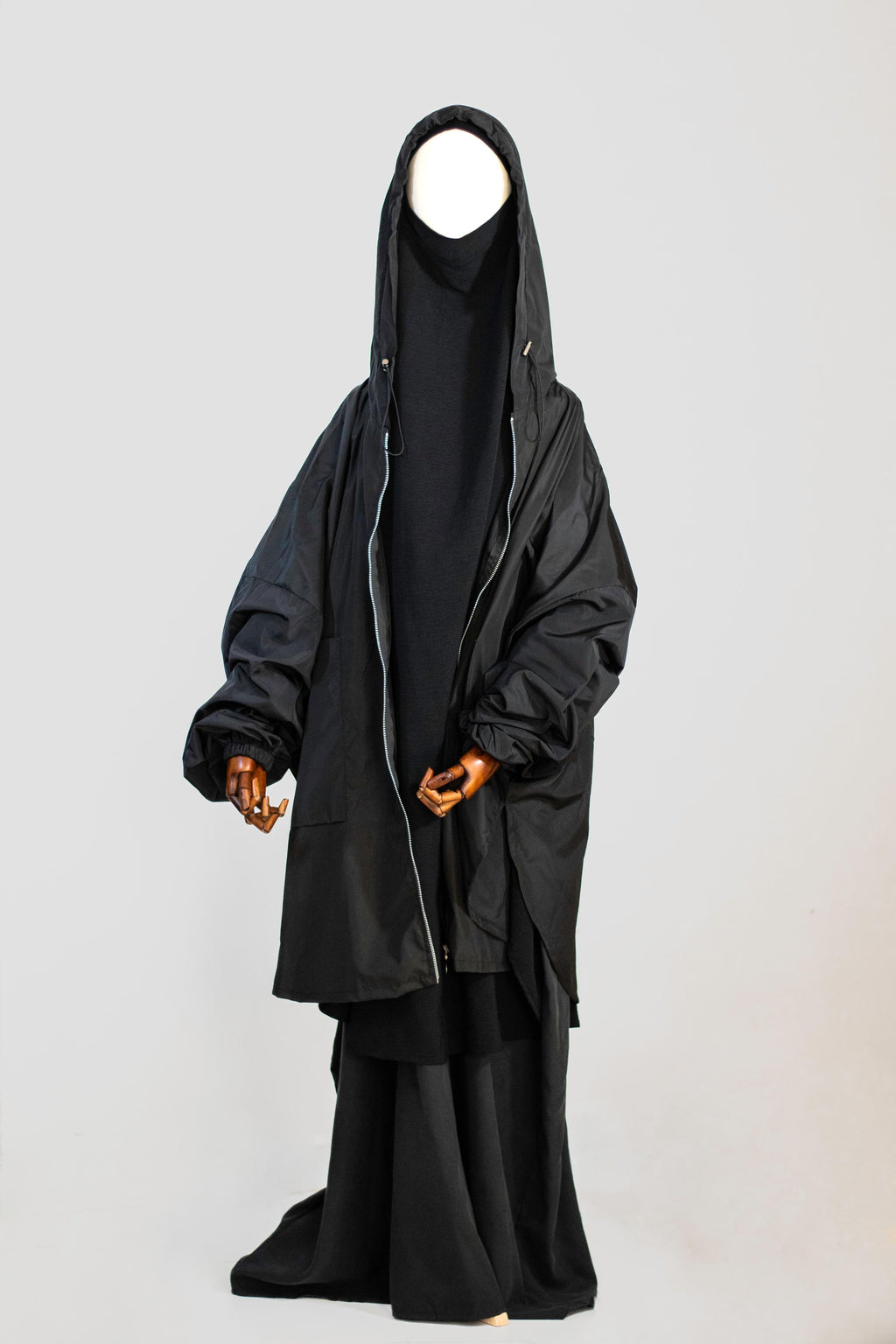 Wijde regenjas Matar in Obsidian zwart van Saahil Collection op houten mannequin met capuchon, minimalistische achtergrond.