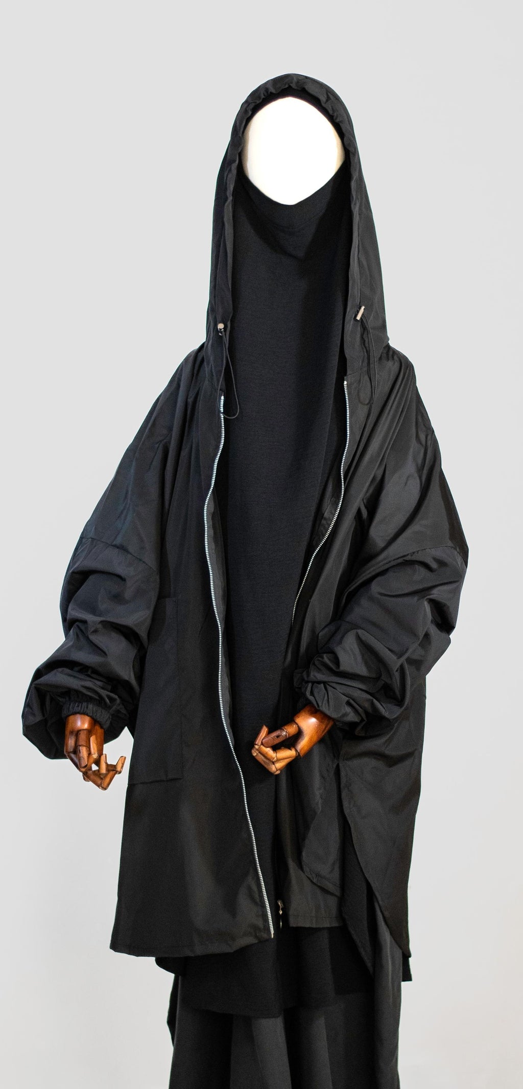 Wijde regenjas Matar in Obsidian zwart van Saahil Collection op houten mannequin met capuchon, minimalistische achtergrond.