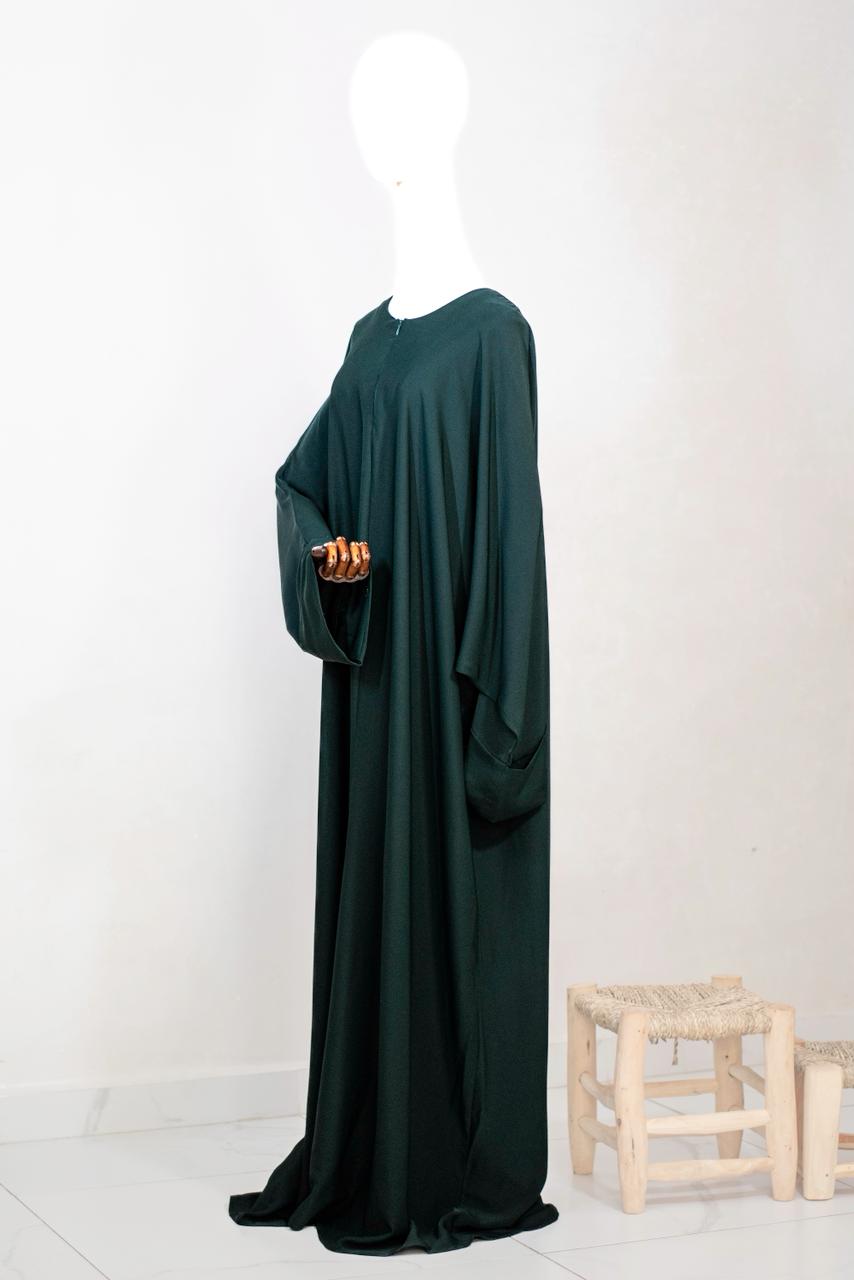 Abaya in midnight green van Saahil Collection, getoond op houten mannequin met wijdvallende mouwen en minimalistische achtergrond.